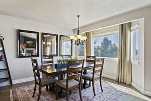 Dining room featuring a textured ceiling, a chandelier, healthy amount of natural light, and dark wood-style floors