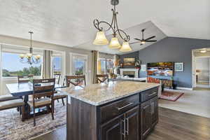 Kitchen with a fireplace, dark brown cabinetry, light stone countertops, pendant lighting, and dark wood-style flooring