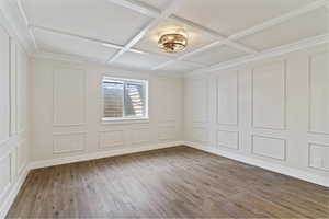 Unfurnished room with a decorative wall, light wood-style floors, coffered ceiling, and beam ceiling
