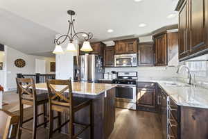Kitchen with pendant lighting, appliances with stainless steel finishes, dark wood-style floors, light stone counters, and a kitchen breakfast bar