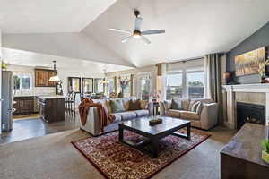 Living area with vaulted ceiling, dark carpet, a tile fireplace, a ceiling fan, and a textured ceiling