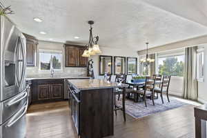 Kitchen with dark brown cabinetry, stainless steel fridge with ice dispenser, a textured ceiling, a kitchen island, and light stone counters