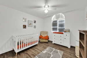 Bedroom with a nursery area, dark wood-style floors, and ceiling fan