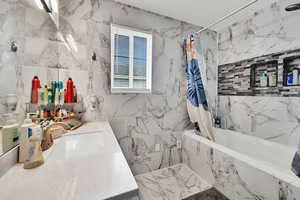 Bathroom with tiled shower / bath, tile walls, and vanity