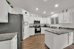 Kitchen featuring dark stone counters, a peninsula, appliances with stainless steel finishes, white cabinetry, and light wood-style flooring