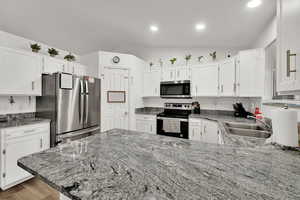 Kitchen featuring lofted ceiling, appliances with stainless steel finishes, white cabinetry, light stone counters, and a peninsula