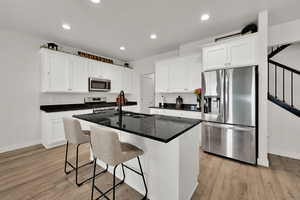 Kitchen with appliances with stainless steel finishes, dark stone counters, a center island with sink, recessed lighting, and white cabinets