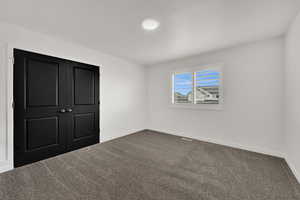 Unfurnished bedroom featuring dark colored carpet and a closet