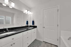 Full bathroom with double vanity, a garden tub, and light wood-type flooring