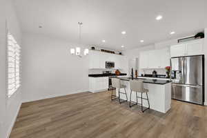 Kitchen featuring appliances with stainless steel finishes, a center island with sink, a breakfast bar area, white cabinetry, and recessed lighting