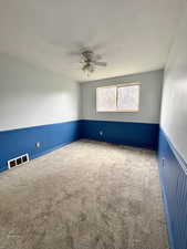 Carpeted spare room featuring a wainscoted wall, a ceiling fan, and a textured ceiling