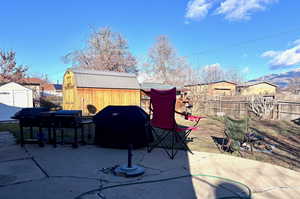 Fenced backyard featuring a storage unit, a grill, and a patio