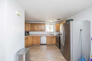Kitchen featuring appliances with stainless steel finishes, light countertops, light wood finished floors, brown cabinets, and a textured ceiling