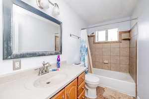 Full bathroom featuring shower / bath combo with shower curtain, vanity, light tile patterned floors, and a textured ceiling