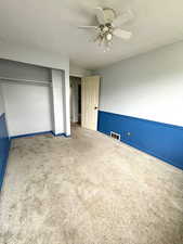 Unfurnished bedroom with carpet, a textured ceiling, ceiling fan, a closet, and a wainscoted wall