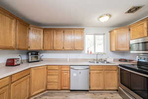 Kitchen featuring appliances with stainless steel finishes, light countertops, light wood finished floors, brown cabinetry, and a textured ceiling