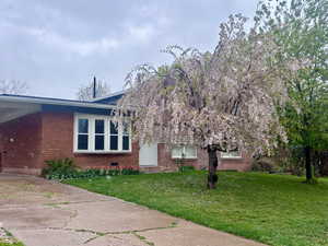 View of property exterior featuring a yard, brick siding, an attached carport, and driveway