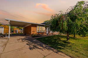 View of front of property with an attached carport, driveway, brick siding, and a shed