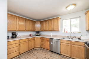 Kitchen with light countertops, stainless steel appliances, light wood-style flooring, a textured ceiling, and brown cabinets