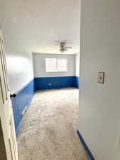 Unfurnished room featuring carpet flooring, ceiling fan, a textured ceiling, and wainscoting