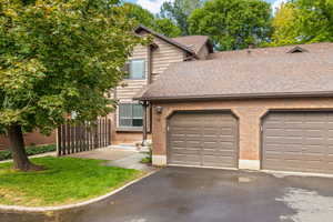 View of front of property featuring front patio, single-car garage, grass area and brick exterior