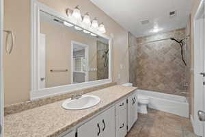 Primary bathroom featuring tile flooring, large vanity, and tiled tub/shower combination