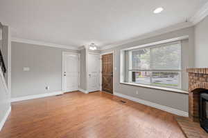 Front entry and living area featuring laminate flooring, two-tone paint, crown molding, bay window, and gas fireplace with brick surround