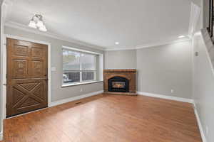 Front entry and living area featuring laminate flooring, two-tone paint, crown molding, bay window, and gas fireplace with brick surround