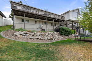 Back of property featuring a trampoline, a lawn, brick siding, and a deck