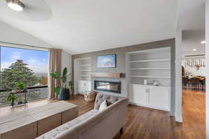 Living room featuring wood finished floors, a glass covered fireplace, and built in shelves