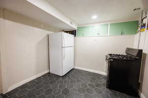 Kitchen with gas stove, freestanding refrigerator, dark tile patterned floors, recessed lighting, and a textured ceiling