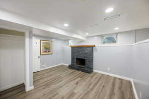 Finished basement featuring wood finished floors, a stone fireplace, and recessed lighting