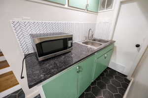 Kitchen with dark tile patterned flooring, dark countertops, backsplash, green cabinets, and stainless steel microwave