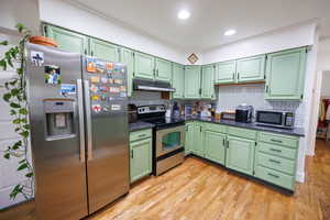 Kitchen with green cabinetry, stainless steel appliances, tasteful backsplash, light wood finished floors, and ornamental molding