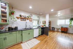 Kitchen with green cabinetry, tasteful backsplash, light wood-style flooring, white dishwasher, and dark stone countertops