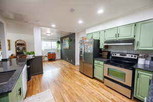Kitchen with green cabinetry, appliances with stainless steel finishes, open floor plan, under cabinet range hood, and light wood finished floors