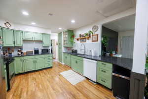 Kitchen with green cabinetry, open shelves, light wood-style flooring, stainless steel appliances, and glass insert cabinets