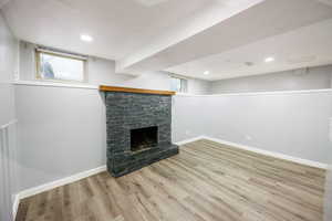 Below grade area with light wood finished floors, a stone fireplace, and recessed lighting