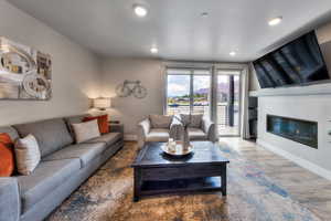 Living area with wood finished floors, a glass covered fireplace, and recessed lighting