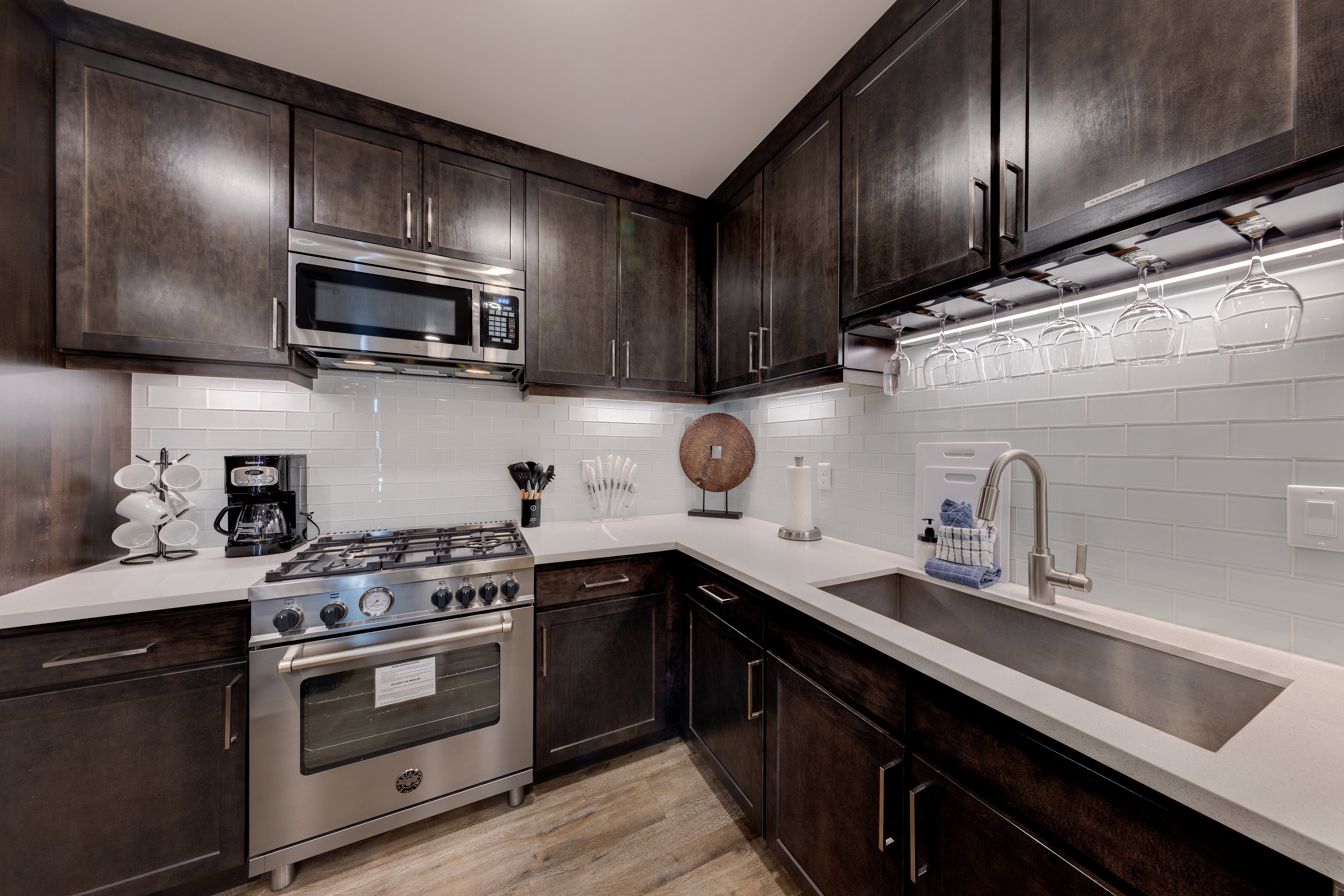Kitchen featuring dark brown cabinets, stainless steel appliances, tasteful backsplash, and light stone counters