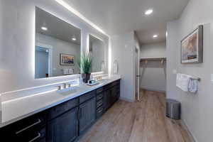 Full bathroom featuring light wood finished floors, double vanity, a spacious closet, and recessed lighting