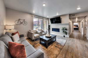 Living area with a glass covered fireplace, wood finished floors, and recessed lighting