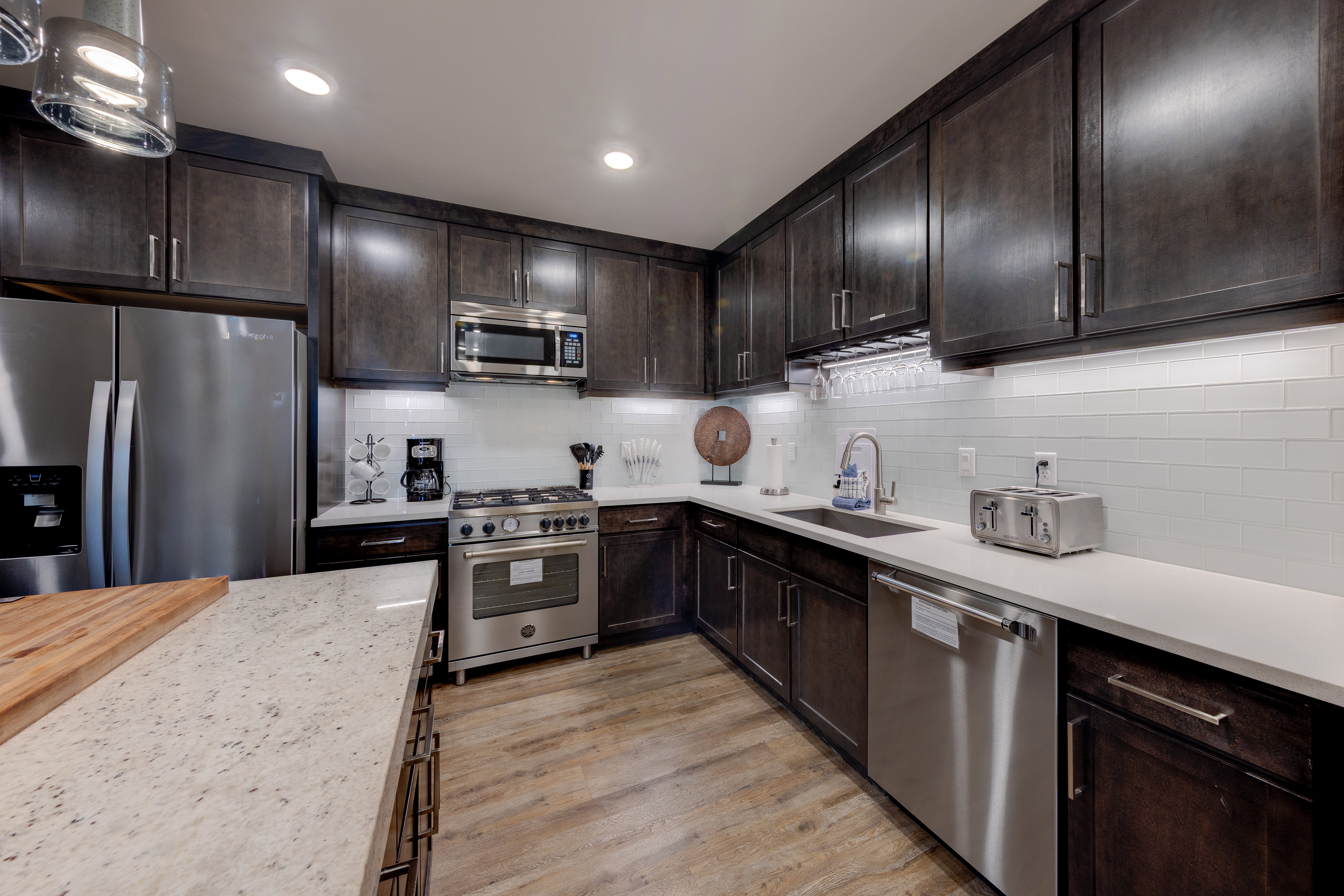 Kitchen featuring dark brown cabinets, stainless steel appliances, tasteful backsplash, light stone counters, and recessed lighting