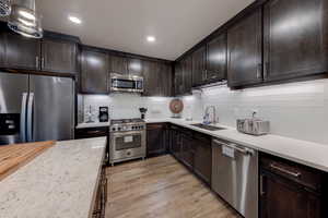 Kitchen featuring dark brown cabinets, stainless steel appliances, tasteful backsplash, light stone counters, and recessed lighting