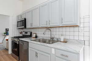 Kitchen featuring light countertops, stainless steel appliances, light wood finished floors, tasteful backsplash, and white cabinetry