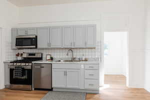 Kitchen with stainless steel appliances, light wood-style floors, light countertops, and decorative backsplash