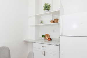 Detailed view of open shelves, freestanding refrigerator, white cabinetry, and light stone countertops