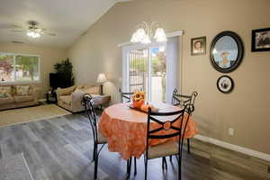 Dining area featuring dark wood-type flooring, vaulted ceiling, ceiling fan, and a chandelier