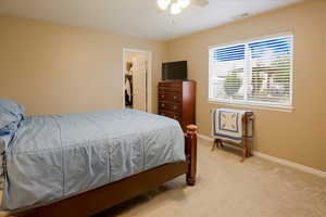 Bedroom featuring light colored carpet, a ceiling fan, and a spacious closet