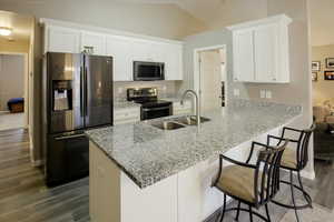 Kitchen with white cabinets, appliances with stainless steel finishes, a kitchen bar, light stone countertops, and a peninsula
